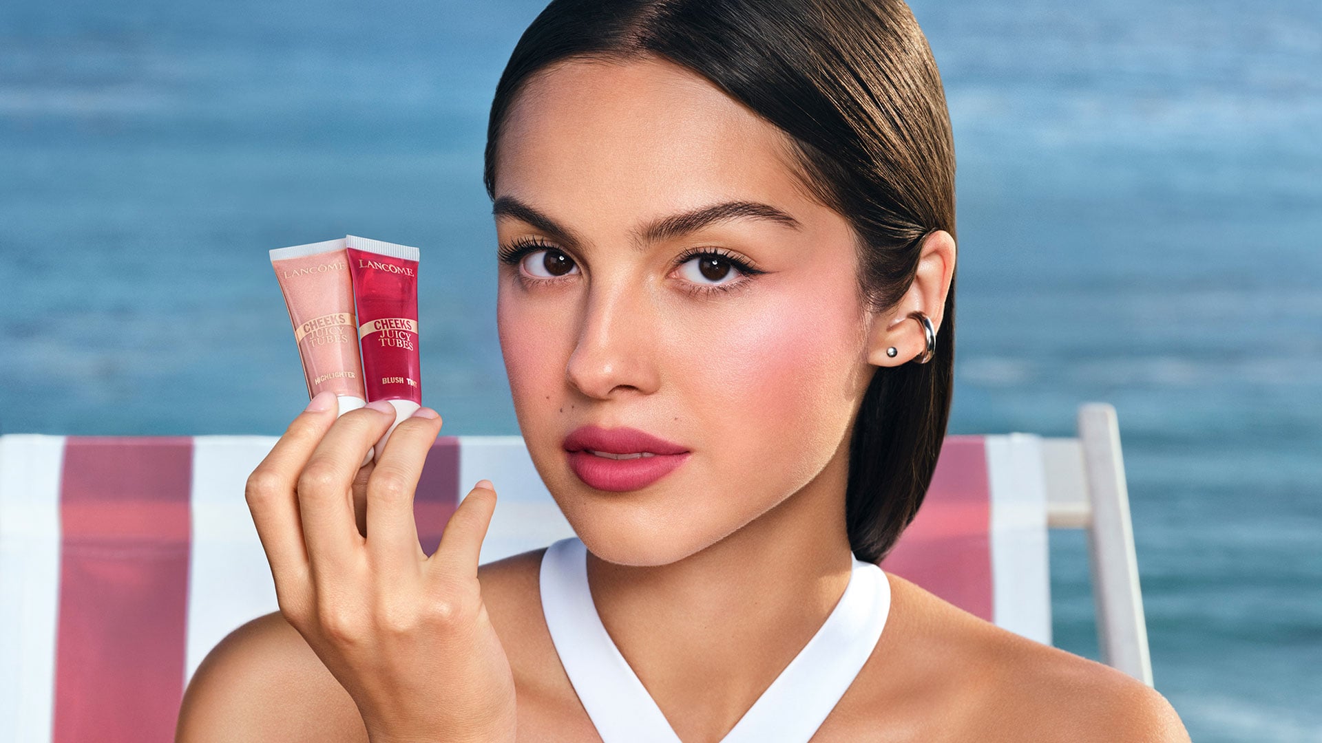 Model holding two Lancôme Juicy Tubes by the sea.